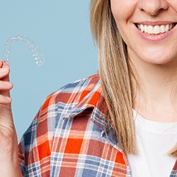 Smiling young woman holding Invisalign aligner