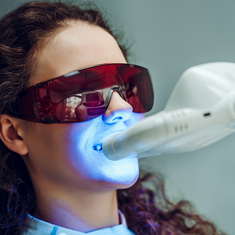 Woman sitting in dental chair receiving teeth whitening