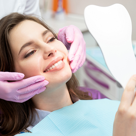 Woman sitting back in dental chair checking smile in handheld mirror