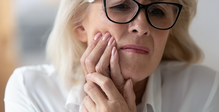 Woman with glasses rubbing jaw in pain in need of emergency dentist in Greenwood Village