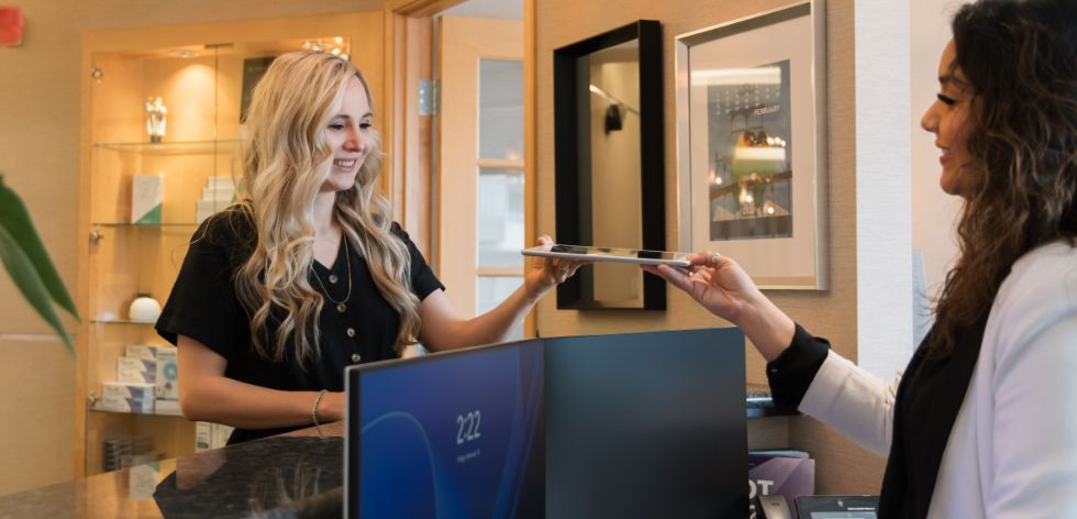 Blonde team member at front desk handing patient a tablet