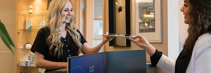 Dental patient at front desk handing tablet to team member